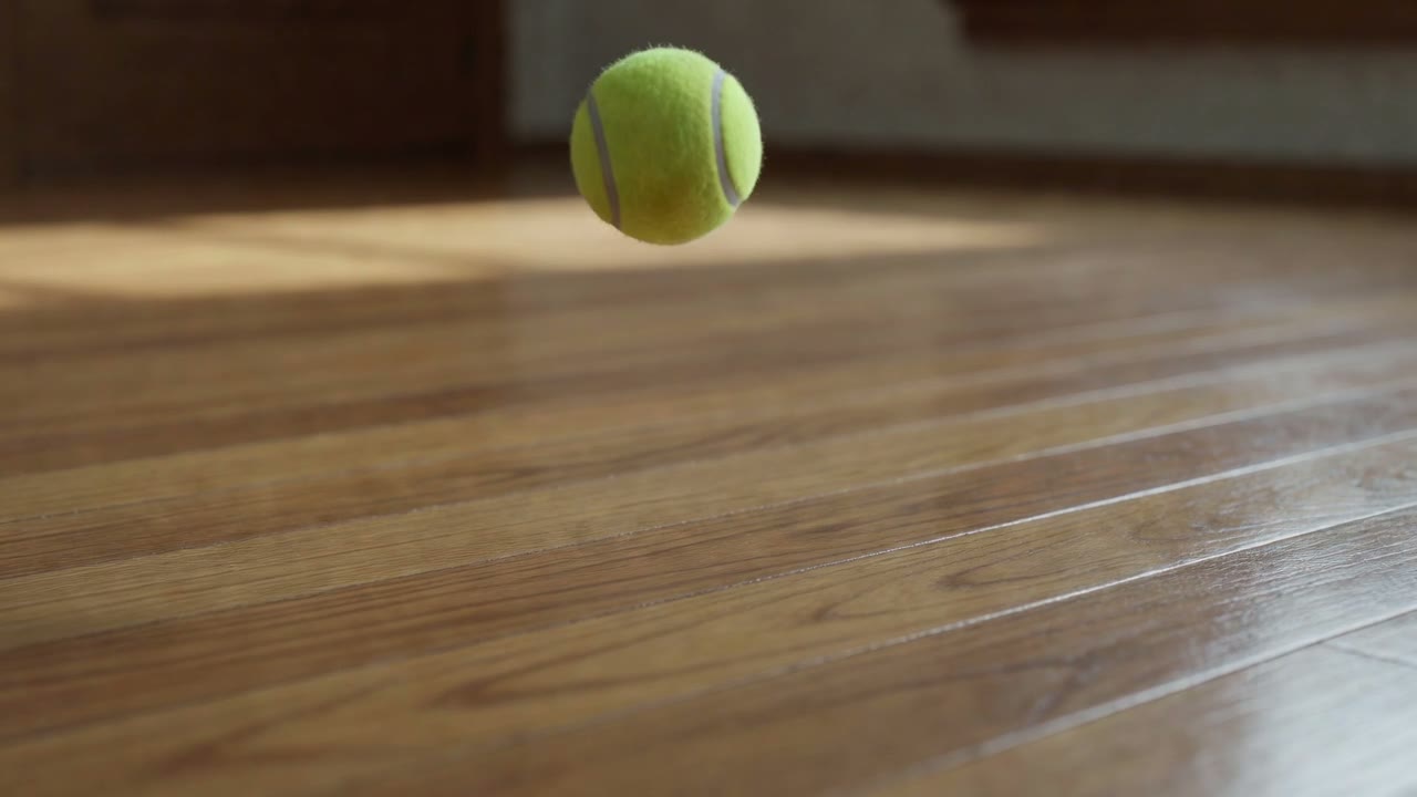 A tennis ball is dropped onto a wooden floor and bounces.